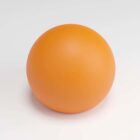 A smooth, round, orange sphere on a light grey surface.