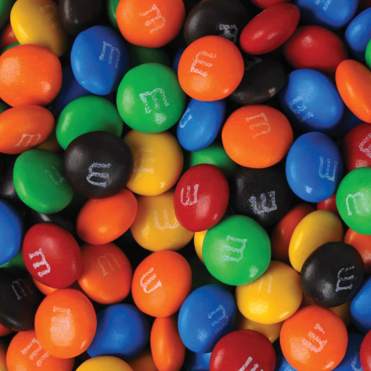 A colorful assortment of M&Ms candies scattered, featuring red, blue, green, orange, yellow, and black pieces.