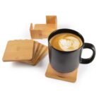 Black mug of latte on a coaster with wooden coasters and holder nearby.