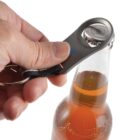 Hand opening a glass bottle with a metal bottle opener on a keychain.