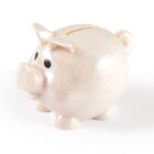 A beige, speckled piggy bank with big eyes, standing on a white background.