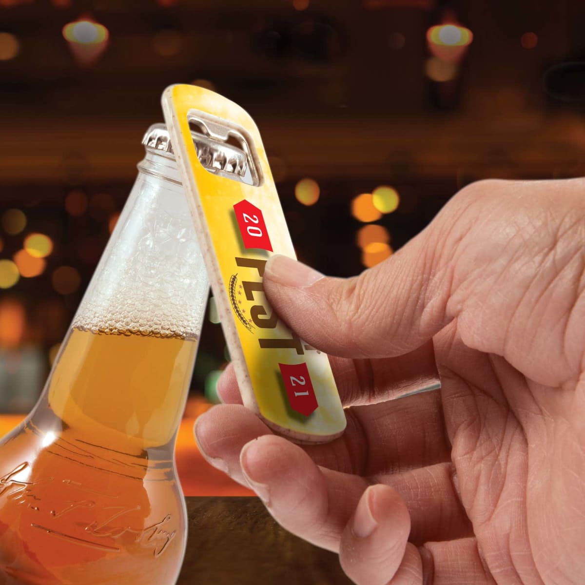 A hand opening a bottle of beer with a bottle opener, against a blurred background with warm bokeh lights.