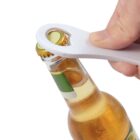 Hand using a white bottle opener to open a glass beer bottle with a golden cap.