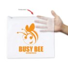 A hand holds a transparent pouch with an orange Busy Bee Learning Centres logo.