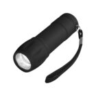Black flashlight with a wrist strap, turned on, illuminating, against a white background.