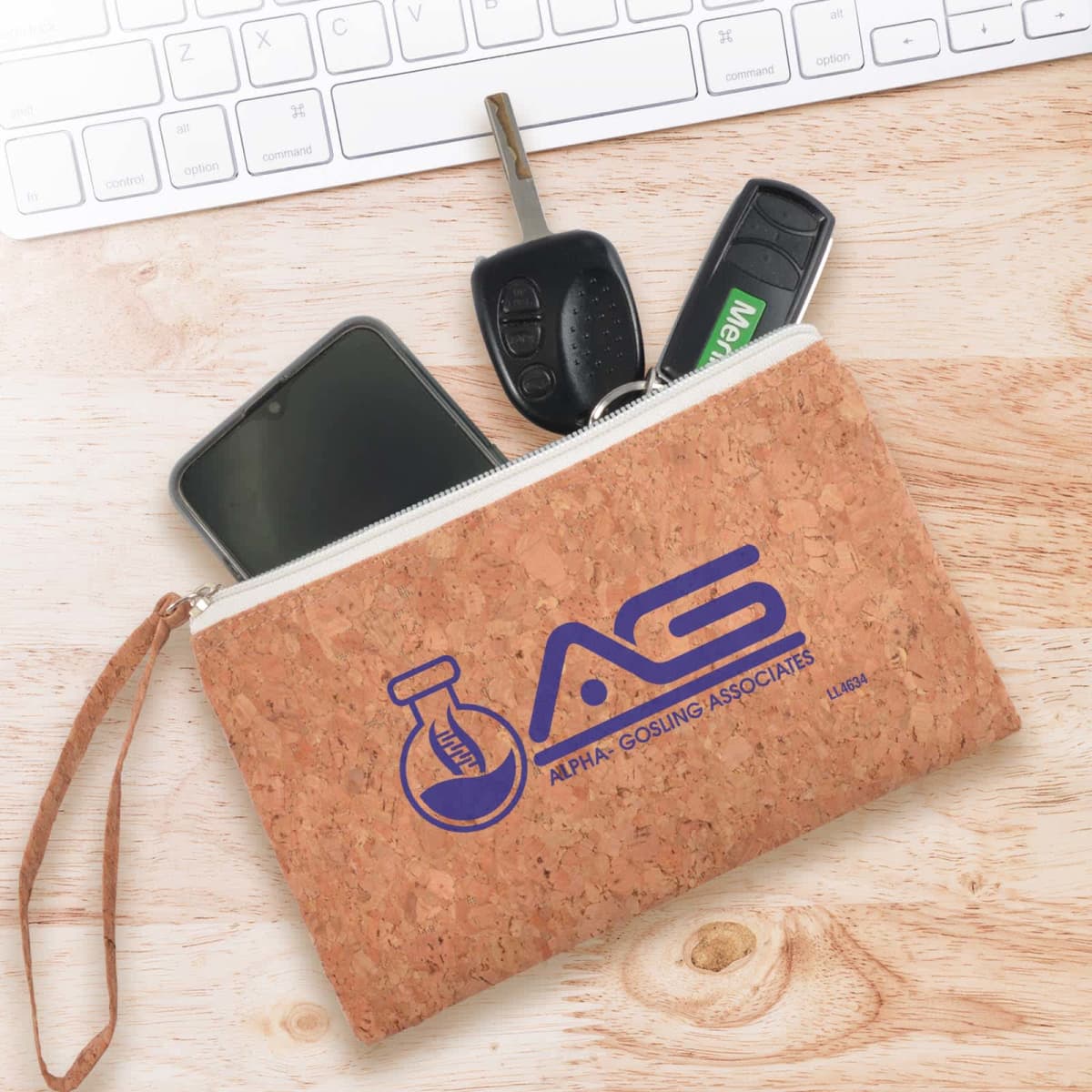 Cork pouch with AG logo, holding a phone, keys, and USB, rests on a wooden surface near a keyboard.