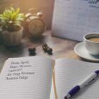 A notebook open on a desk lists agenda items like meeting agenda and budget allocation. Beside it is a pen, a white coffee cup, a plant, an old-fashioned alarm clock, and a calendar in the background.