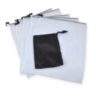 Five white mesh laundry bags with black drawstring closures are spread out, with a smaller black pouch positioned on top of them.