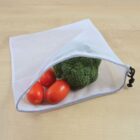 A reusable mesh produce bag partially open on a wooden surface containing a broccoli head and three red Roma tomatoes.
