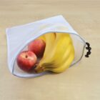 A white mesh bag containing a bunch of bananas and two red apples is placed on a wooden surface.