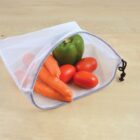 Reusable mesh produce bag partially open on a wooden surface, containing three carrots, three red tomatoes, and one green bell pepper.