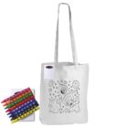 A white tote bag with black outlines showing a rocket, Earth, and stars. Next to the bag is a set of crayons in various colors. The bag is designed for coloring.