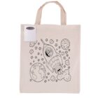 A beige tote bag featuring a black outline design of a rocket, planets, and stars. The bag includes a small attached pack of colorful markers for coloring the design.