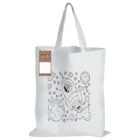 A canvas tote bag featuring a black and white illustration of a dog in a rocket ship. The background has stars, clouds, and a planet resembling Earth. A small set of four colored crayons is attached to the bag.