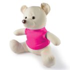 A stuffed teddy bear with cream-colored fur sits upright, wearing a bright pink shirt. The bear has a dark brown nose and black eyes, with its arms and legs slightly spread. The background is plain white.