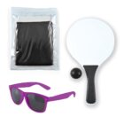 A paddle ball game set with a white paddle, black ball, purple sunglasses, and a black mesh bag in a clear plastic case.