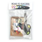 A clear plastic bag labeled Road to Success contains a small spiral notebook, pen, and assorted candies, including jelly beans and chocolates. The design features road signs in various colors.