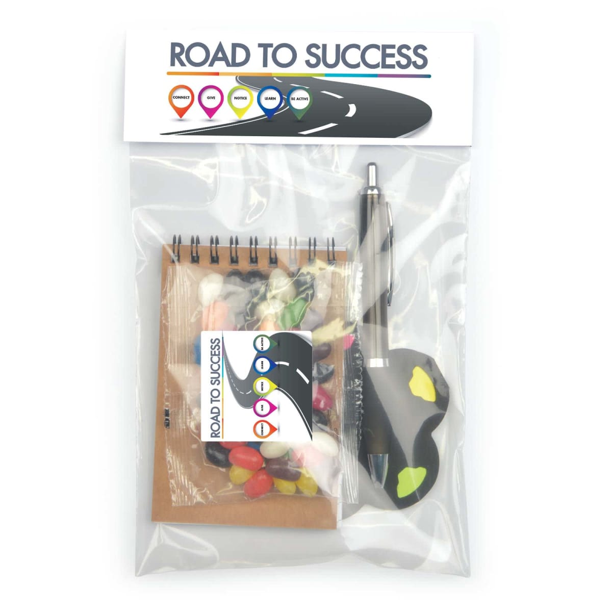 A clear plastic bag labeled Road to Success contains a small spiral notebook, pen, and assorted candies, including jelly beans and chocolates. The design features road signs in various colors.