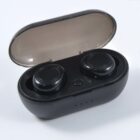 A pair of black wireless earbuds in an open charging case, placed against a plain white background. The case is oval-shaped, and the earbuds are securely nestled inside.