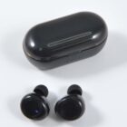 A pair of black wireless earbuds placed in front of their matching black oval charging case on a white background.