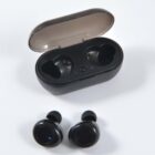 A pair of black wireless earbuds placed in front of an open black charging case. The case is designed to fit and charge the earbuds, with two slots labeled L and R for left and right. The lid is semi-transparent and slightly tilted back.