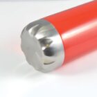 A close-up of a red cylindrical object lying on its side with a shiny, reflective metallic bottom. The smooth red surface contrasts with the textured metallic base. The background is plain white.