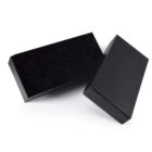 Two rectangular black boxes, one standing upright and the other lying flat. The boxes have a sleek, minimalist design, with smooth surfaces and sharp edges.