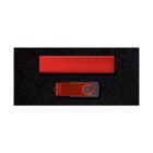 A red USB flash drive with a swivel cover lies on a black surface, accompanied by a separate rectangular red object above it.