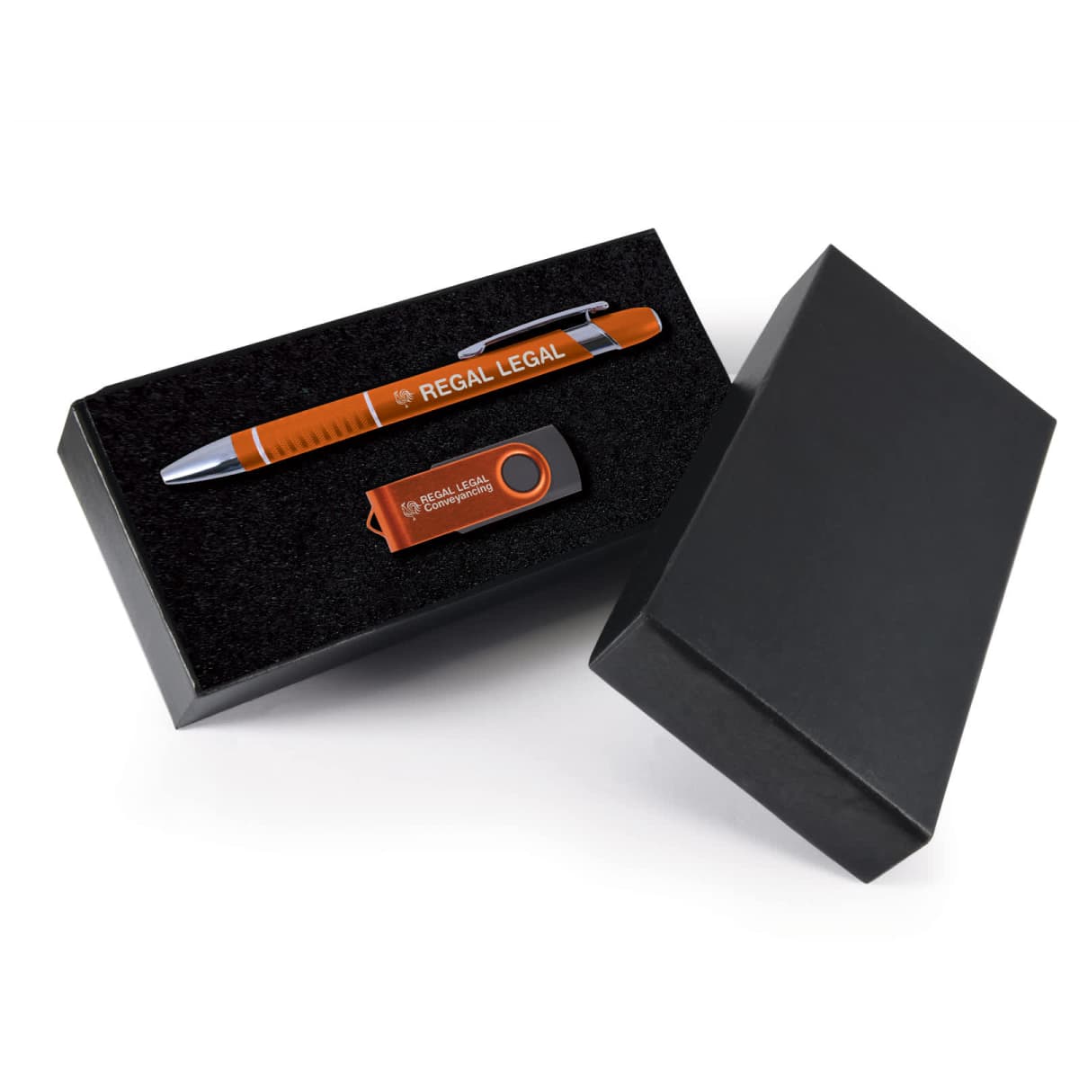 A black gift box containing a metallic orange pen labeled REGAL LEGAL and a matching USB flash drive marked with REGAL LEGAL CORPORATION. The boxs lid is partially open, showing the foam interior.
