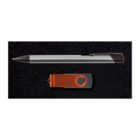 A silver and black pen lies above an orange and gray USB flash drive on a black textured surface.