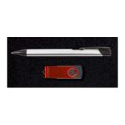 A silver and black pen and a red USB flash drive are placed side by side on a black textured surface.