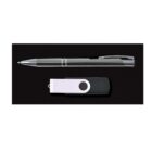 A silver and black pen is positioned above a black and white USB flash drive on a dark surface.