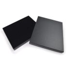 Two black rectangular boxes on a white background, one partially open showing its lid and the other closed. The boxes have a sleek, smooth surface, suggesting a modern and minimalistic design.