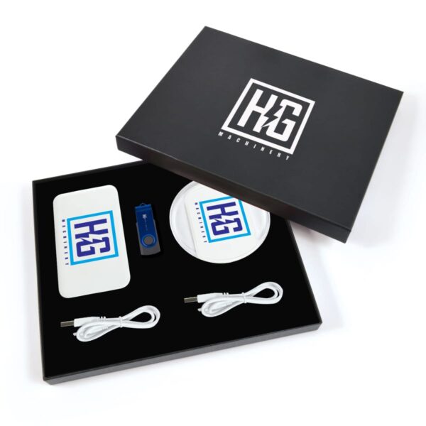 Open black box revealing branded merchandise including a power bank, a wireless charger, a USB flash drive, and two charging cables. All items feature a blue and white logo with the letters HG Machinery.