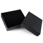 A black rectangular box with its lid partially open, revealing an empty interior. The box is positioned on a white surface with a slight shadow.
