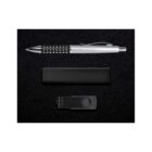 A pen with a silver body and black grip, a rectangular black object, and a black USB flash drive with a swivel cover are arranged on a black surface.