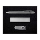 A gift set on a black surface containing a silver pen, a rectangular power bank, and a silver USB flash drive.