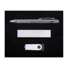 A silver pen, a rectangular silver power bank, and a white USB flash drive with a black circular accent are neatly arranged on a black background.