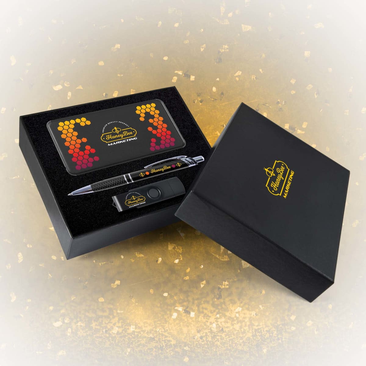 A black gift box containing a pen, USB drive, and a notebook with a honeycomb design. The items have HoneyBee Marketing branding in yellow on them. The box is open and displayed on a textured, gradient background.