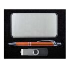 A metal business card holder, an orange pen with a silver clip, and a USB drive with a silver swivel cover are arranged against a black background.