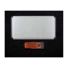 A rectangular metal case and a USB flash drive with an orange cover and a circular hole are placed on a black textured surface.