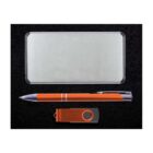 A rectangular silver metal box with rounded edges, an orange and silver pen, and an orange USB flash drive are neatly arranged on a black surface.