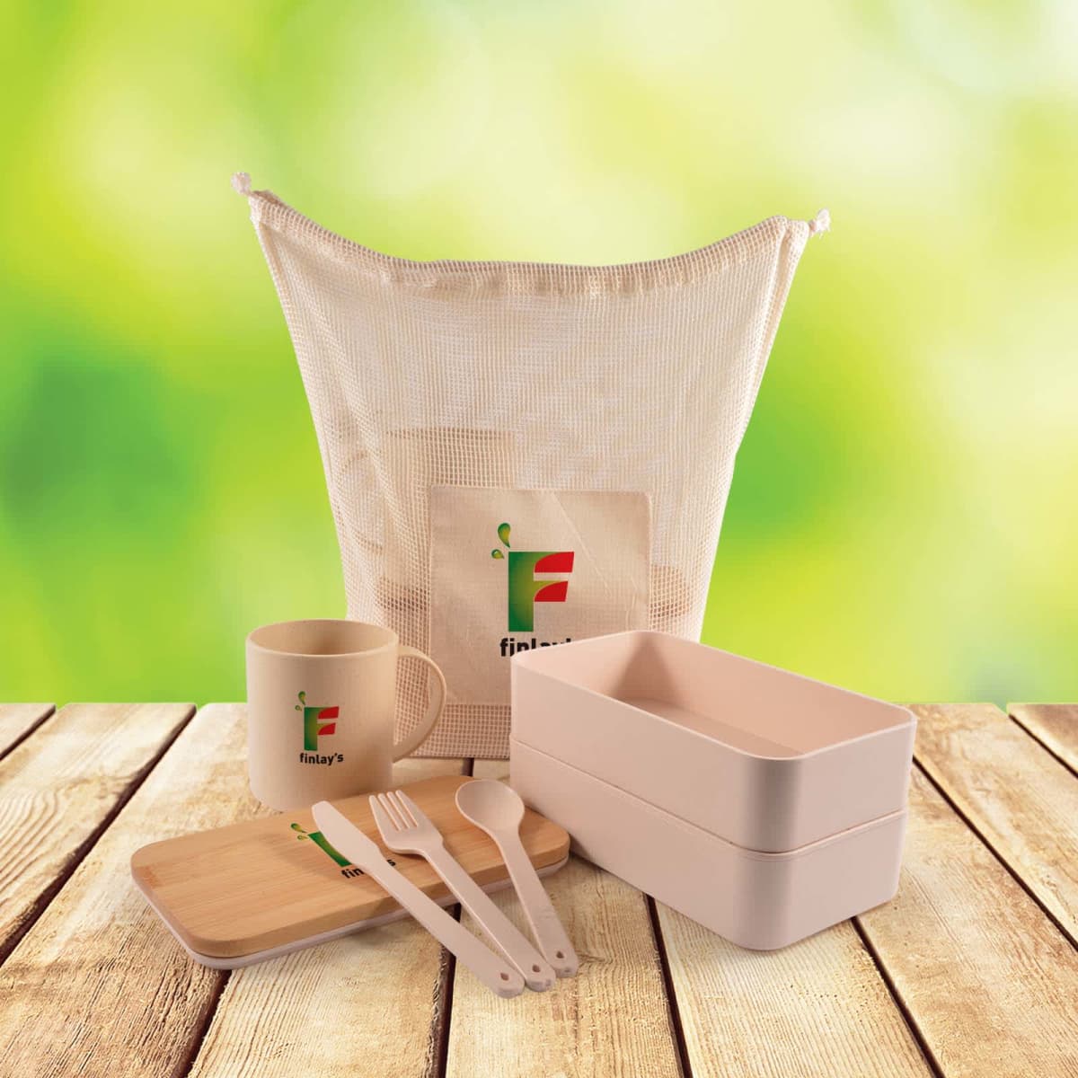 Eco-friendly dining set with a beige bento box, wooden utensils, a mug, and a bamboo lid, all branded with a logo. Items are displayed on a wooden surface against a blurred green background.