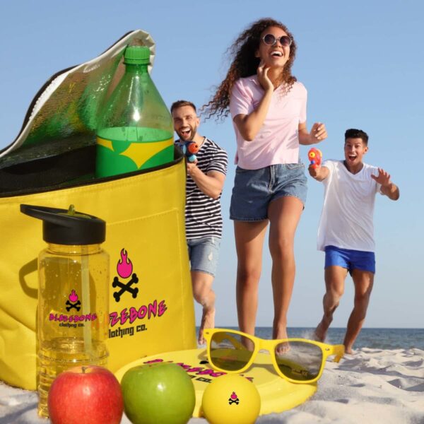 Three people are enjoying a sunny beach day. In the foreground, there are apples, a bottle, and sunglasses on the sand. A yellow cooler with a soda bottle is open. One person is holding a water pistol, smiling and running towards the camera.