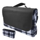 A black and white plaid picnic blanket folded into a portable form with a black flap and handle for easy carrying. An additional rolled-up view of the blanket is shown in the bottom left corner.