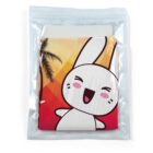 A sealed plastic bag contains a colorful cloth with a cartoon bunny illustration. The bunny is smiling with closed eyes against a background of red, orange, and yellow gradients with a silhouette of a palm tree.