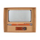 A cardboard gift box containing a metal business card holder, an orange pen with silver accents, and an orange and black USB drive.