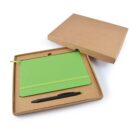A green notebook and a black pen inside an open kraft box. The box is on a white background, with the notebook positioned diagonally and the pen placed below it. The lid of the box is partially removed and leaning against the box.