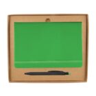 A green notebook with an elastic band is placed in a brown cardboard package. Below the notebook is a black pen with a green tip.