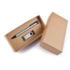Open cardboard box containing a black and silver pen and a silver USB flash drive with a swivel cover inside. The lid is placed to the right of the box.